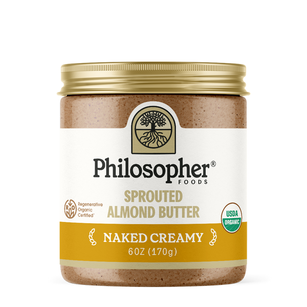Image displays front of jar. Label displays image of tree with roots, "Philosopher Foods" in bold black text, "Sprouted Almond Butter" in gold, "Naked Creamy" in white, 6 ounce jar. Also shows label icons for USDA Certified organic and for Regenerative Organic Certified
